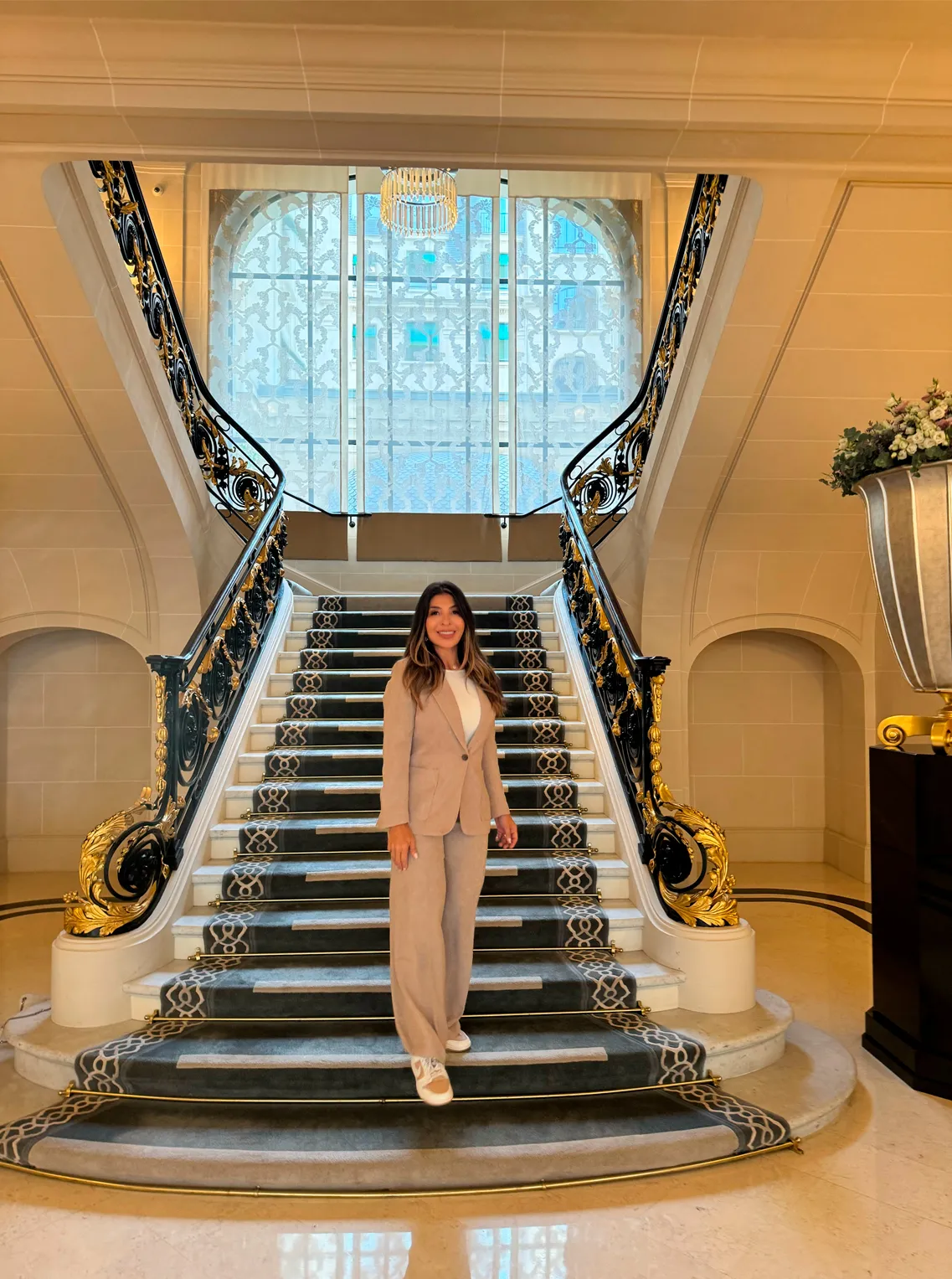 Woman in a beige suit on a grand marble staircase beneath a stained-glass window