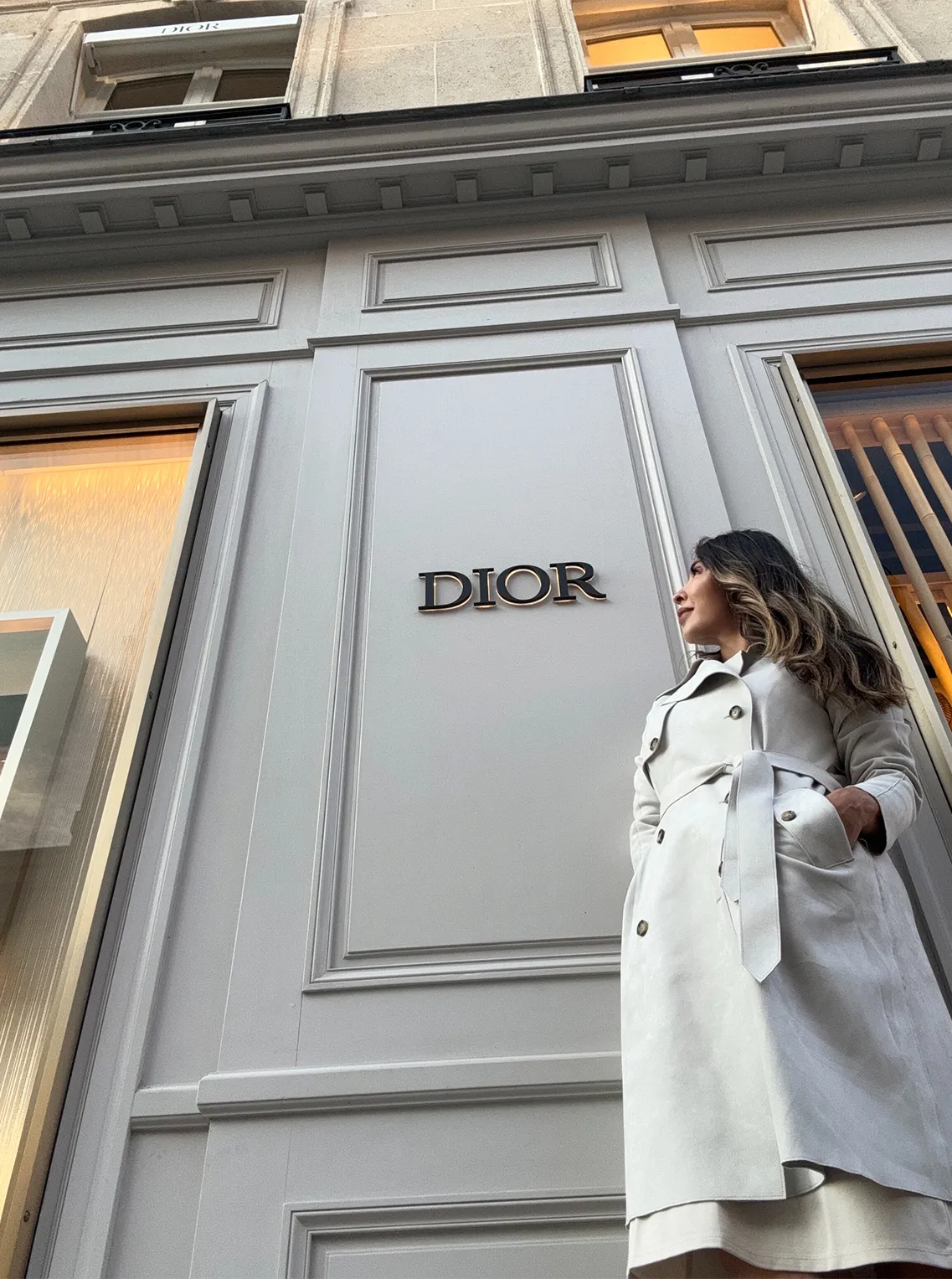 Woman in a white trench coat standing outside a Dior boutique