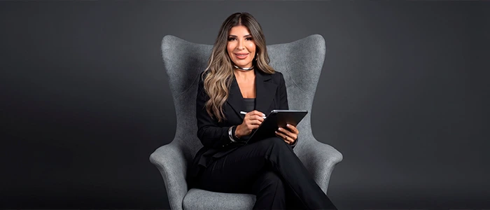 Smiling woman in black seated in a gray wingback chair, holding a tablet